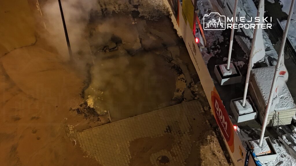 Para ludzi stojąca obok otwartego włazu, z którego wydobywa się para, w otoczeniu śnieżnego krajobrazu.