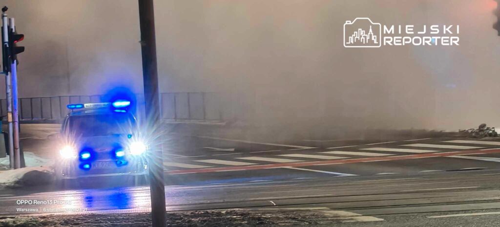 Policyjny radiowóz z niebieskimi sygnałami świetlnymi stoi na ulicy w gęstej mgle.