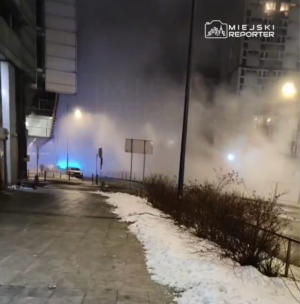 Mgła otacza niebieskie światła radiowozu na ośnieżonym chodniku w mieście nocą.