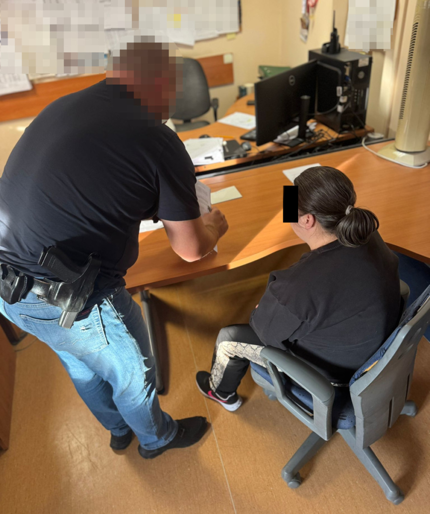 Mężczyzna w mundurze rozmawia z kobietą siedzącą przy biurku w pomieszczeniu biurowym.