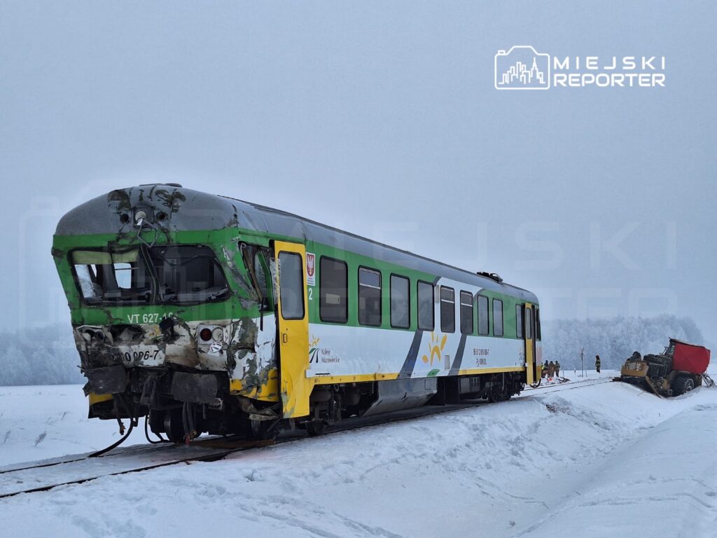 Zniszczony pociąg stojący na zaśnieżonym torowisku, obok pracujący zespół ratunkowy.