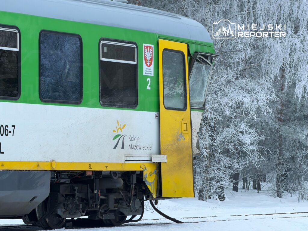 Pociąg Kolei Mazowieckich na tle zaśnieżonego lasu, z widoczną zamrożoną szybą i żółtym detalem drzwi.