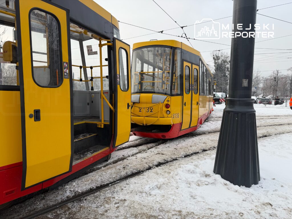 Tramwaj w żółto-czerwonym malowaniu zatrzymany na przystanku, z otwartymi drzwiami, w zaśnieżonym otoczeniu.