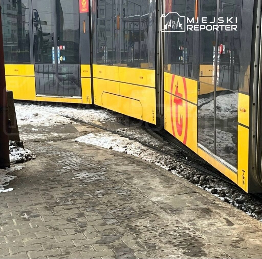 Żółty tramwaj skręca na zakręcie na śliskiej, ośnieżonej nawierzchni.