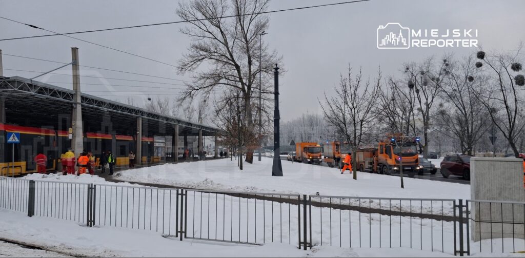 Grupa pracowników w odblaskowych kamizelkach pracuje przy przystanku tramwajowym w zimowej scenerii.
