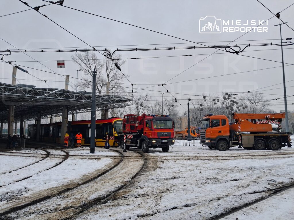 Grupa pracowników w odblaskowych kamizelkach obserwuje akcję ratunkową tramwajów w zimowym otoczeniu.