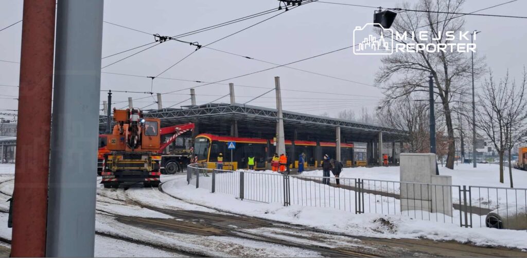 Ekipa pracowników w kamizelkach odblaskowych przeprowadza prace przy nowoczesnej zajezdni tramwajowej w zimowej scenerii.