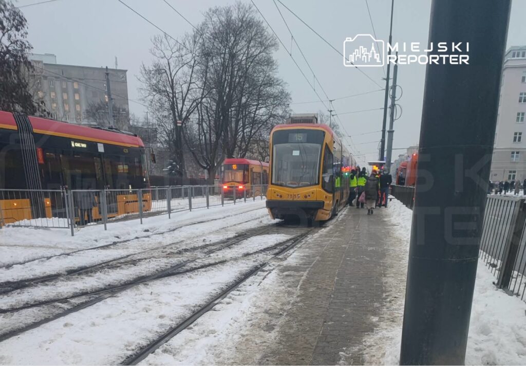Tramwaj zatrzymany na przystanku, a pasażerowie wchodzą i wychodzą w zimowej scenerii z zalegającym śniegiem.
