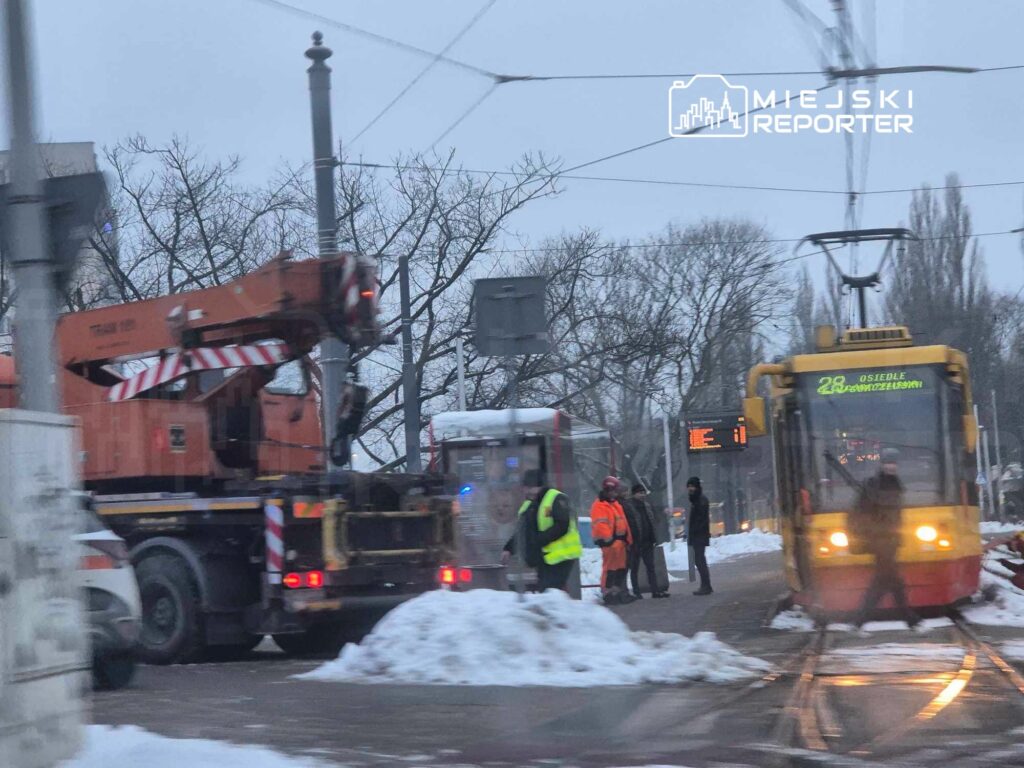 Ekipa pracowników w pomarańczowych kamizelkach prowadzi prace przy torowisku tramwajowym w zimowym otoczeniu.