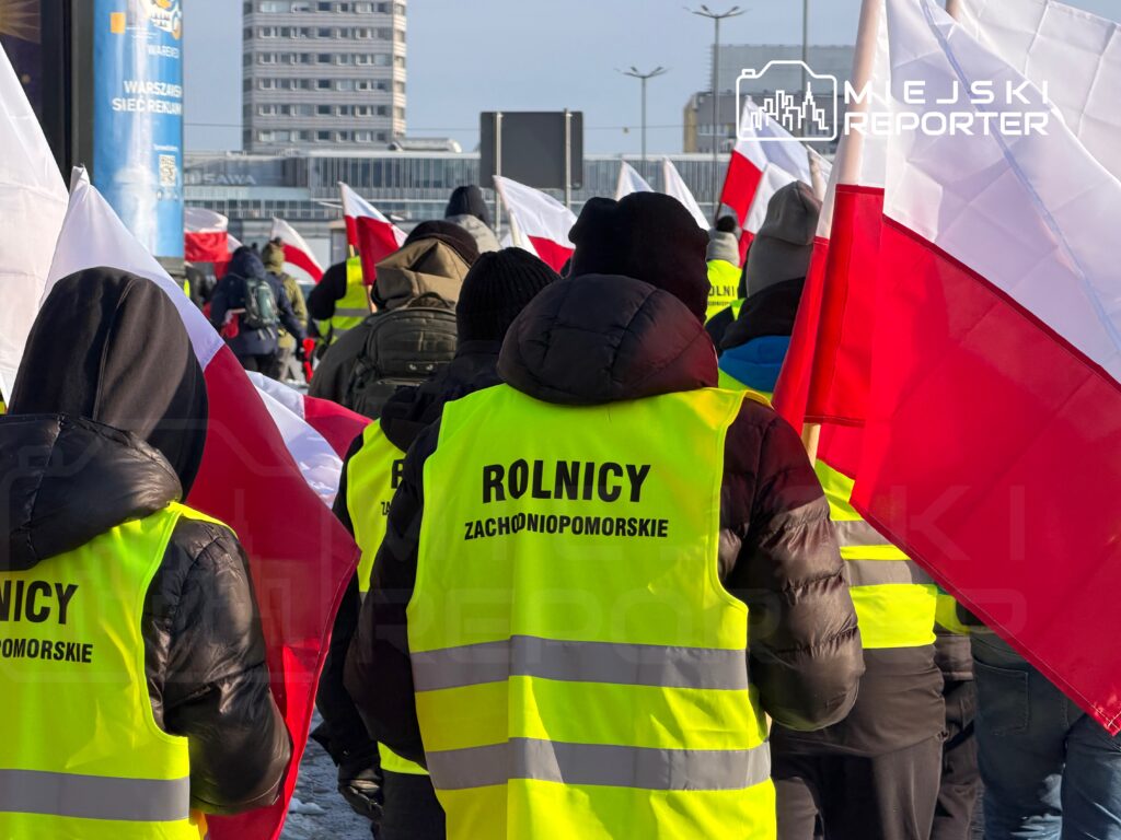 Grupa rolników w żółtych kamizelkach z napisami "ROLNICY ZACHODNIOPOMORSKIE" trzyma flagi Polski podczas protestu.