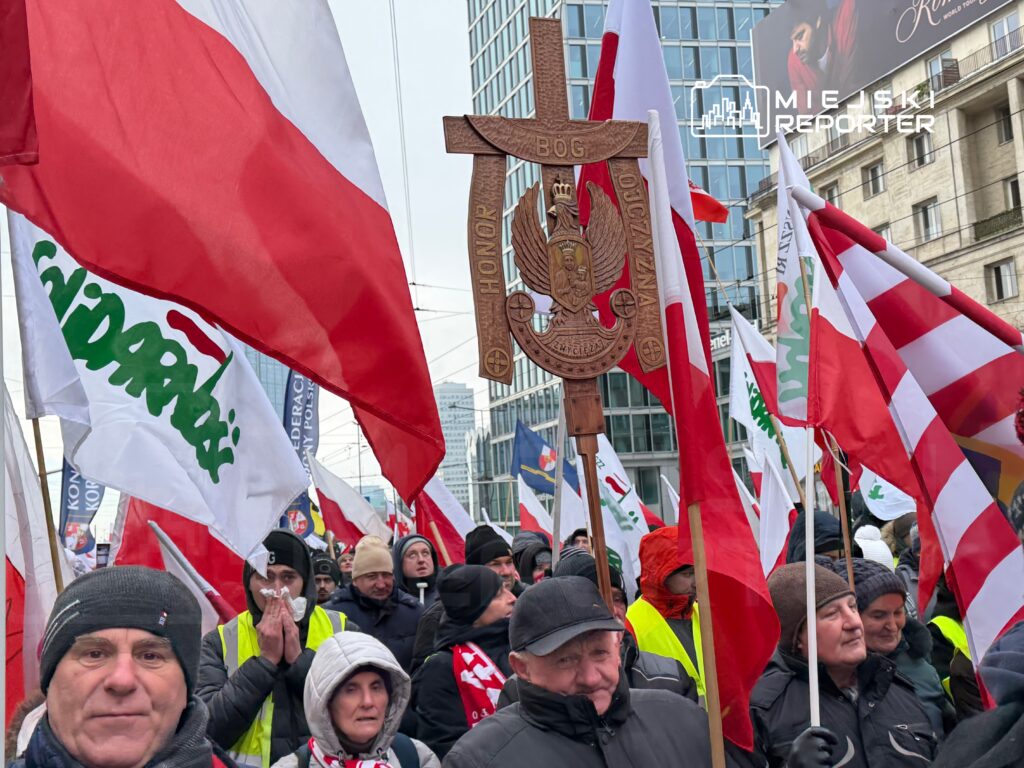 Tłum ludzi niosący flagi Polski i transparenty, w tym z napisem "Solidarność", podczas demonstracji w miejskim centrum.