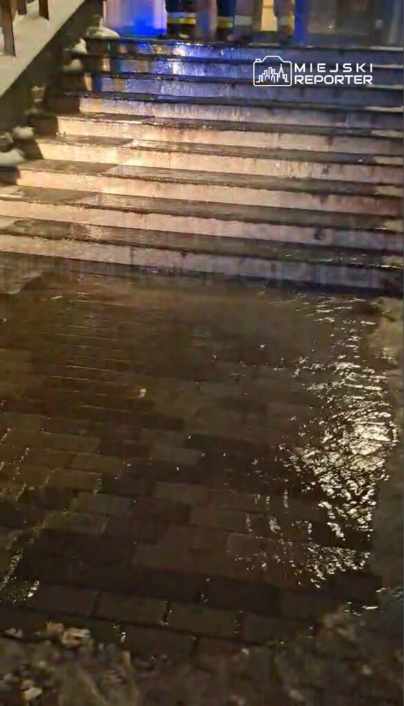 Woda gromadzi się na schodach pokrytych kostką brukową w ciemnym otoczeniu, odbijając światło.