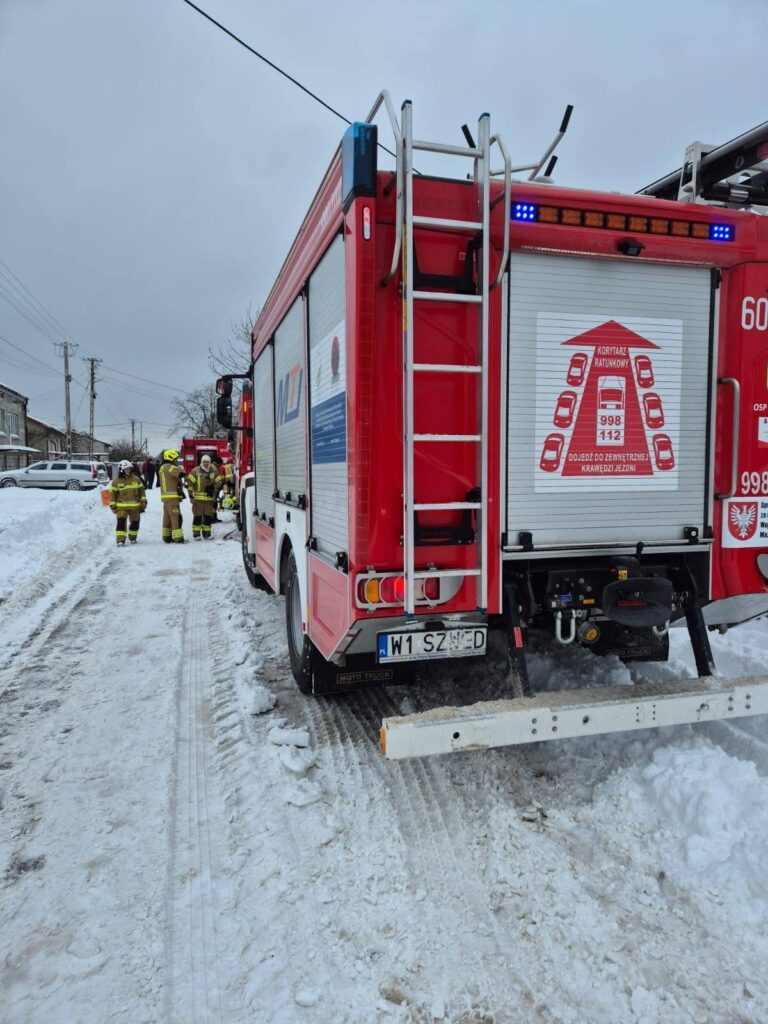Strażacy w mundurach omawiają sytuację obok wozu strażackiego na zaśnieżonej ulicy.