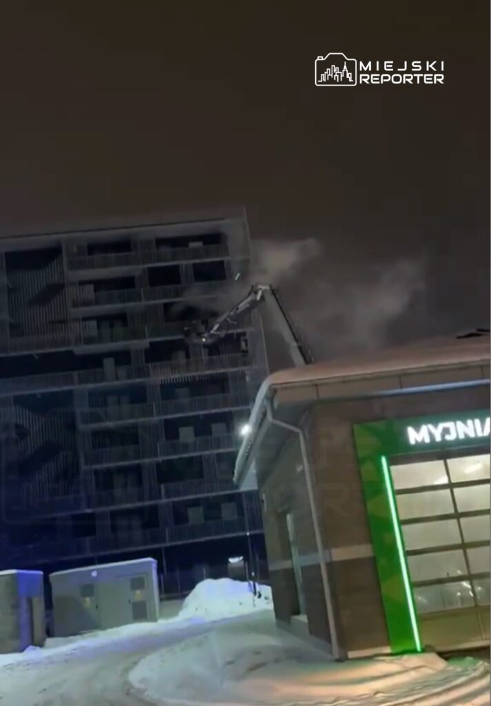 Pracownik na wysięgniku wykonuje prace na elewacji nowoczesnego budynku mieszkalnego w zimowej scenerii.