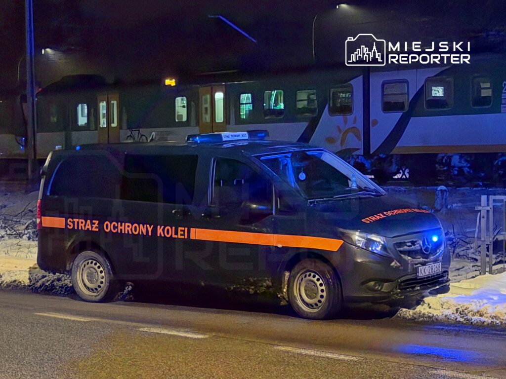 Samochód Straży Ochrony Kolei zaparkowany przy torach kolejowych w nocy, z włączonymi sygnalizatorami.