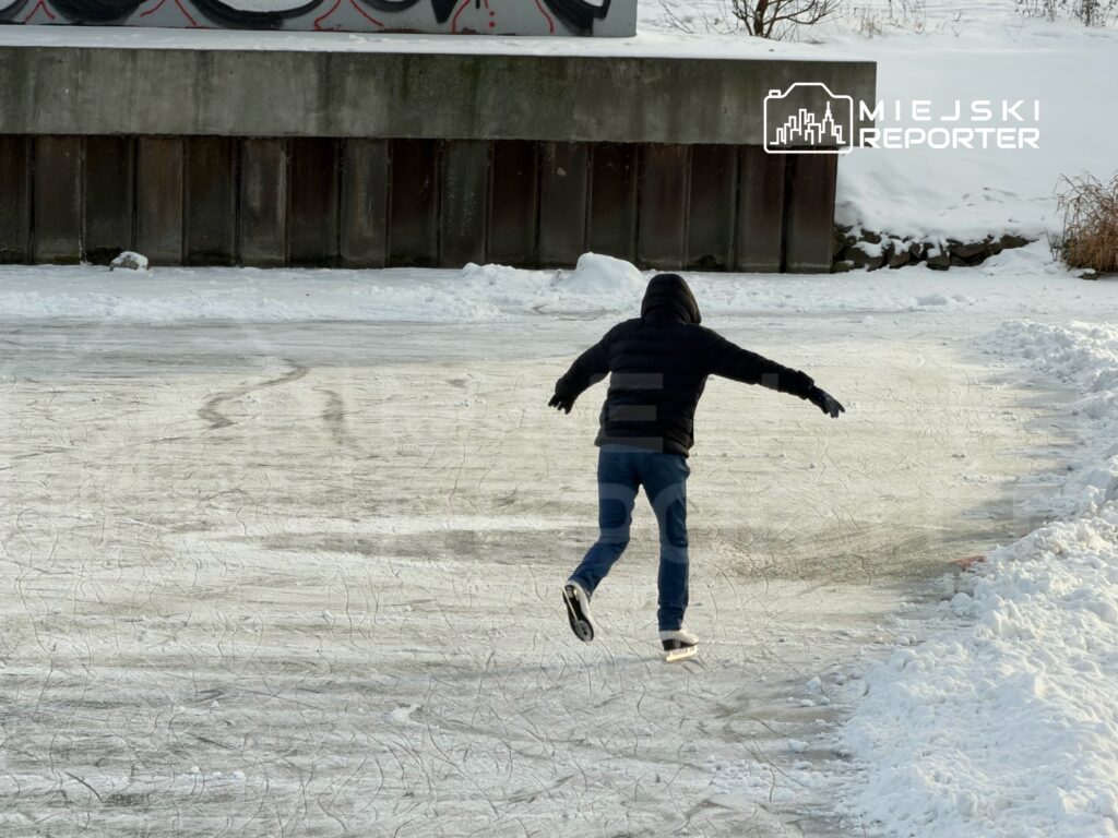 Chłopiec w czarnej kurtce ślizga się na łyżwach po zamarzniętej tafli lodu, otoczony śniegiem.