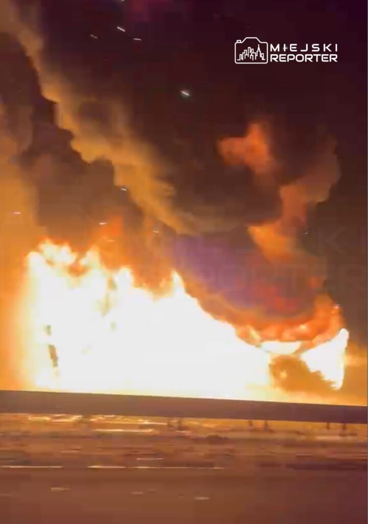 Intensywny pożar z dużymi płomieniami oraz gęstym dymem unoszącym się w nocy nad drogą.