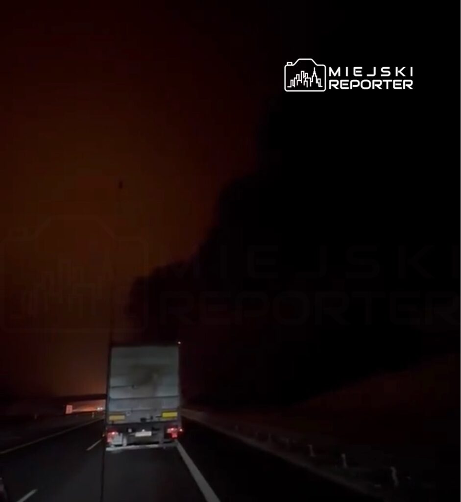 Ciemny dym unoszący się nad autostradą, widoczny za ciężarówką na drodze.