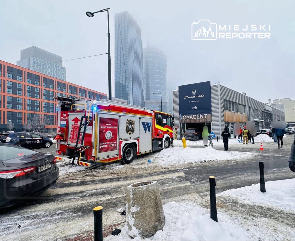 Straż pożarna z włączonymi sygnałami manewruje w śniegu przed nowoczesnym budynkiem z oznaczeniem "Maserati Warszawa".
