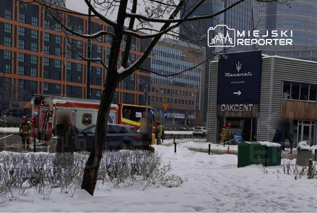 Strażacy w mundurach pracują przy wozie strażackim obok budynku w zimowej scenerii, w otoczeniu śniegu.