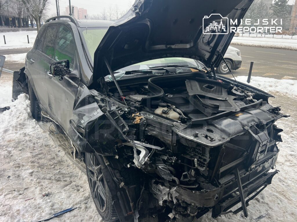 Uszkodzone czarne SUV z otwartą maską, stojące na zaśnieżonej drodze, z widocznymi uszkodzeniami z przodu.