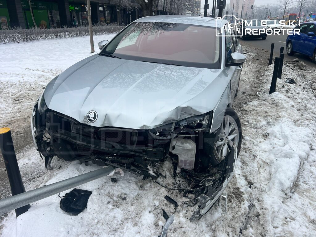 Zniszczony samochód osobowy na poboczu, z wgniecionym przodem i uszkodzoną felgą, obok leży metalowy słup.