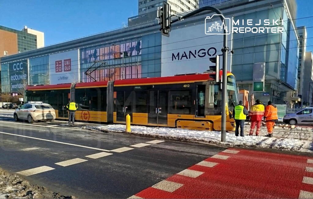 Tramwaj z numerem 4012 zatrzymany na przystanku, obok grupy pracowników w odzieży roboczej, w miejskim otoczeniu.