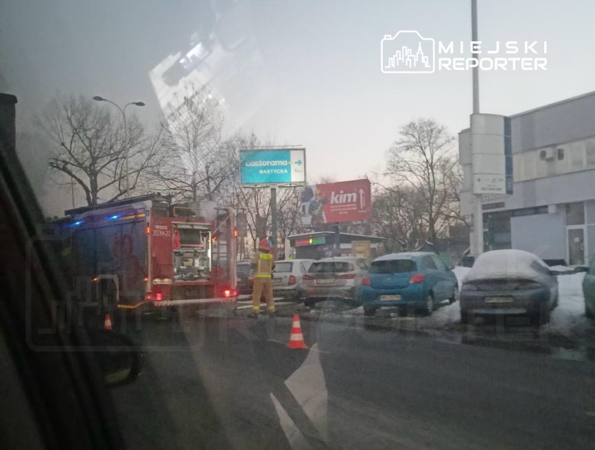 Straż pożarna z włączonymi sygnałami i strażak w kamizelce ostrzegawczej pracują na ruchliwej ulicy w zimowej scenerii.