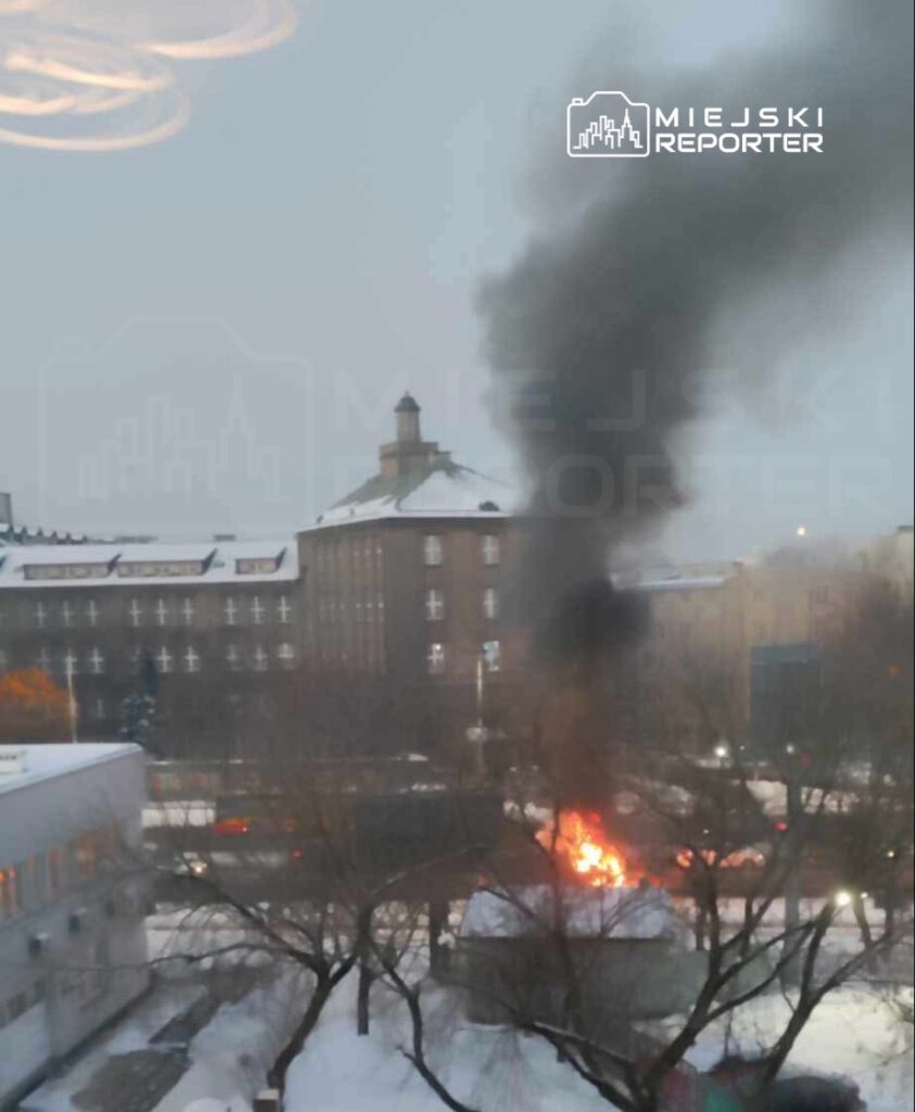 Ogień wydobywający się z budynku w miejskim otoczeniu, z gęstym czarnym dymem unoszącym się w powietrzu.