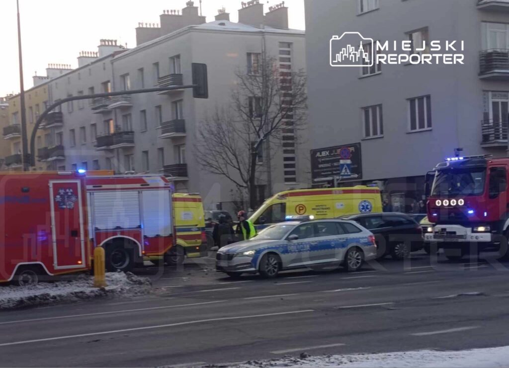 Karetka pogotowia i wóz strażacki stoją na ulicy, obok policyjny radiowóz, w tle budynki mieszkalne.