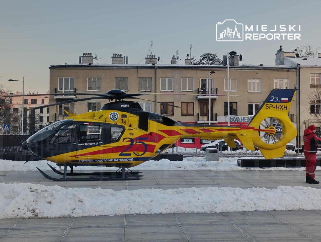 Śmigłowiec ratunkowy w żółto-czerwonych barwach stoi na placu pokrytym śniegiem, obok niego ratownik medyczny.