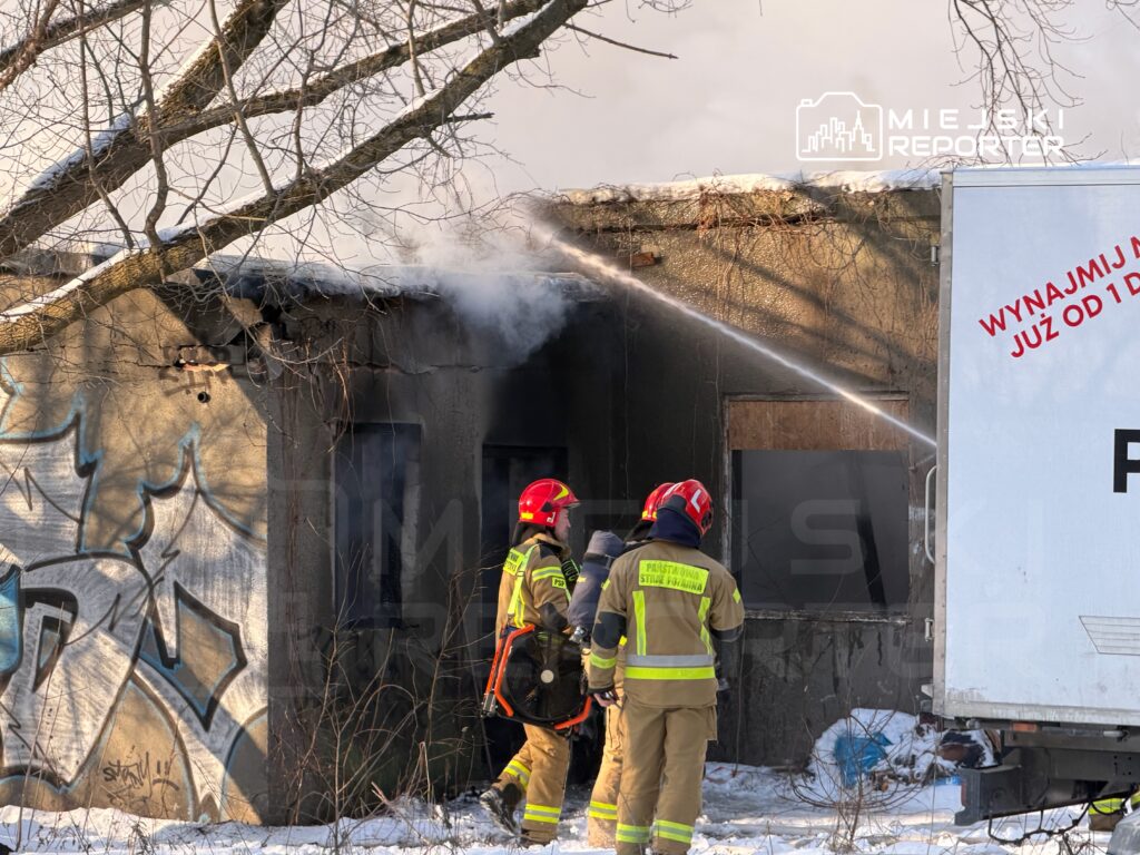 Strażacy gaszą pożar w zniszczonym budynku pokrytym graffiti, w otoczeniu zimowej scenerii.