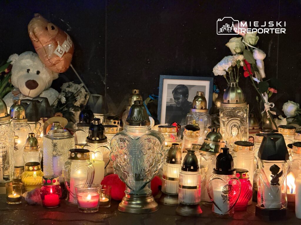 Znicze w różnych kształtach i kolorach wokół zdjęcia, pluszowy miś i balon z napisem "BĄDŹ".