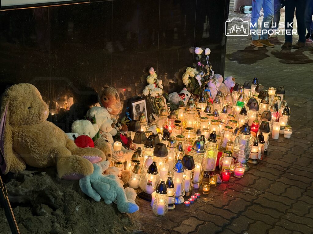 Miejsce pamięci z pluszakami, zniczami i kwiatami, ustawione przy ścianie. W tle widoczny portret.