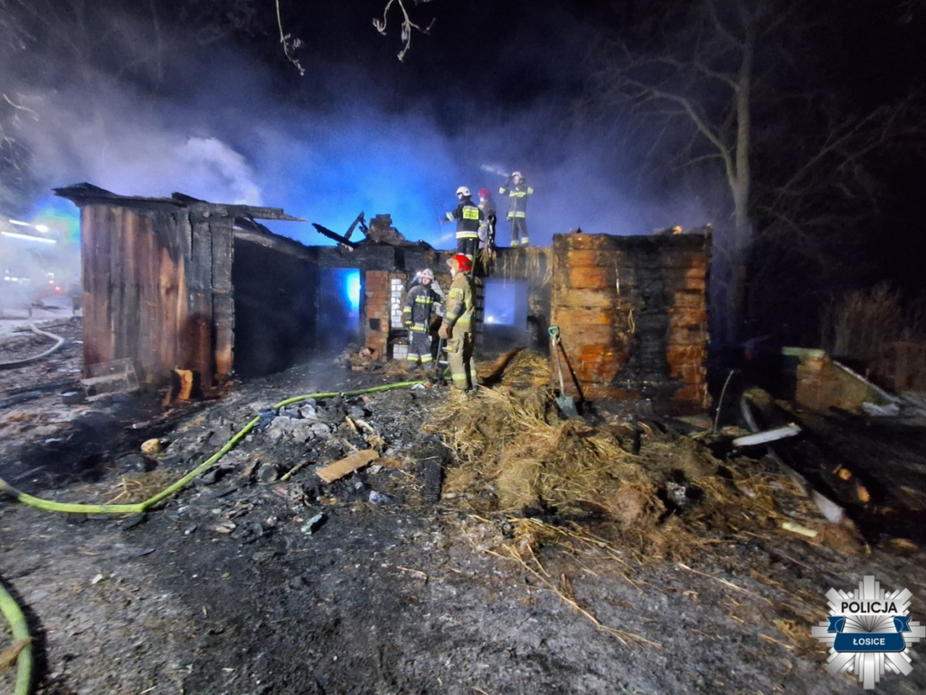Strażacy gaszą pożar zniszczonego budynku w nocy, w otoczeniu dymu i popiołu.
