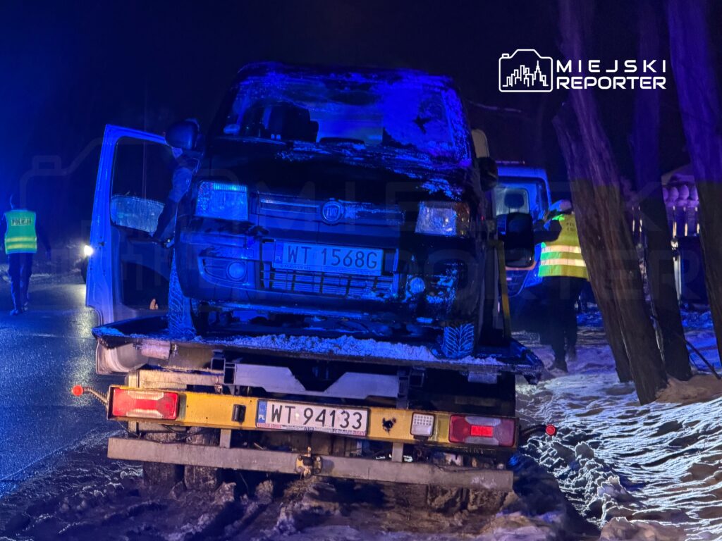 Czarny samochód osobowy wciągany na lawecie przez pracowników służb ratunkowych w nocy, w otoczeniu śniegu.