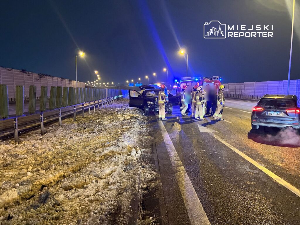 Grupa strażaków udziela pomocy poszkodowanym przy zderzeniu dwóch samochodów na drodze w nocy.