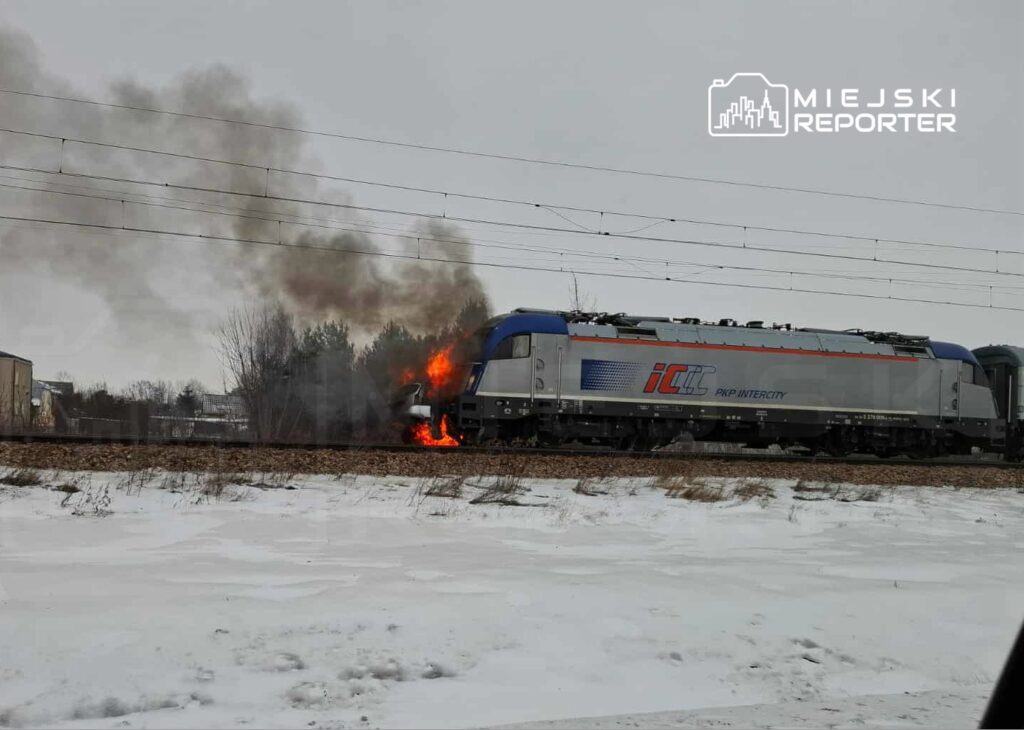 Pociąg PKP Intercity stoi na torach, wydobywa się z niego dym i płomienie, w tle widoczne zalesienie.