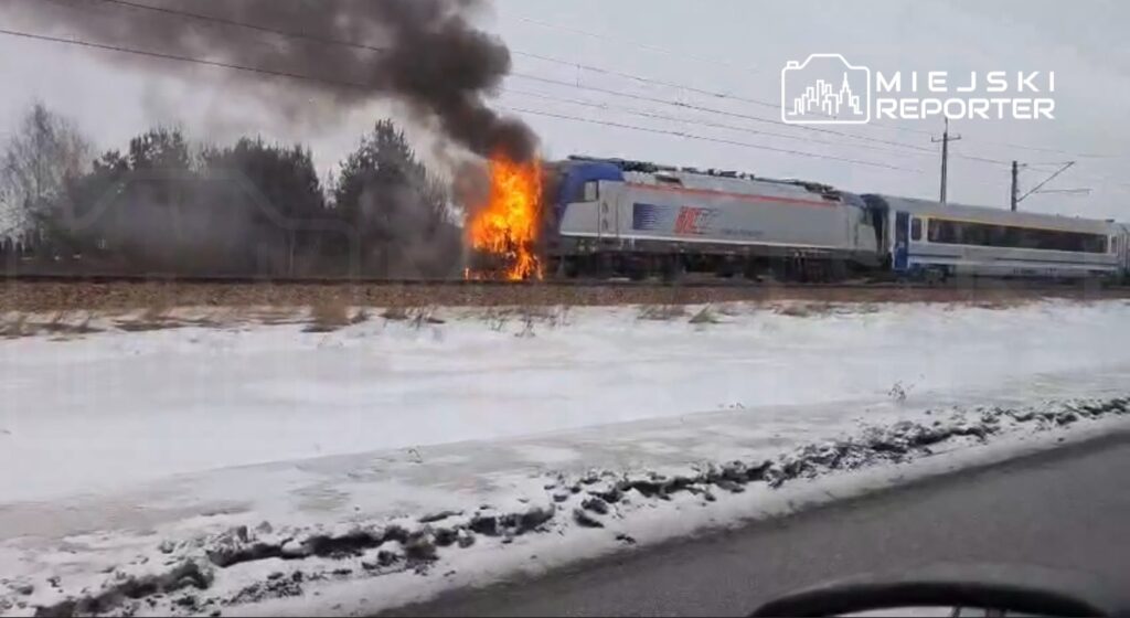 Pociąg towarowy wydobywa dym i ogień z przodu, przejeżdżając obok zaśnieżonego terenu.