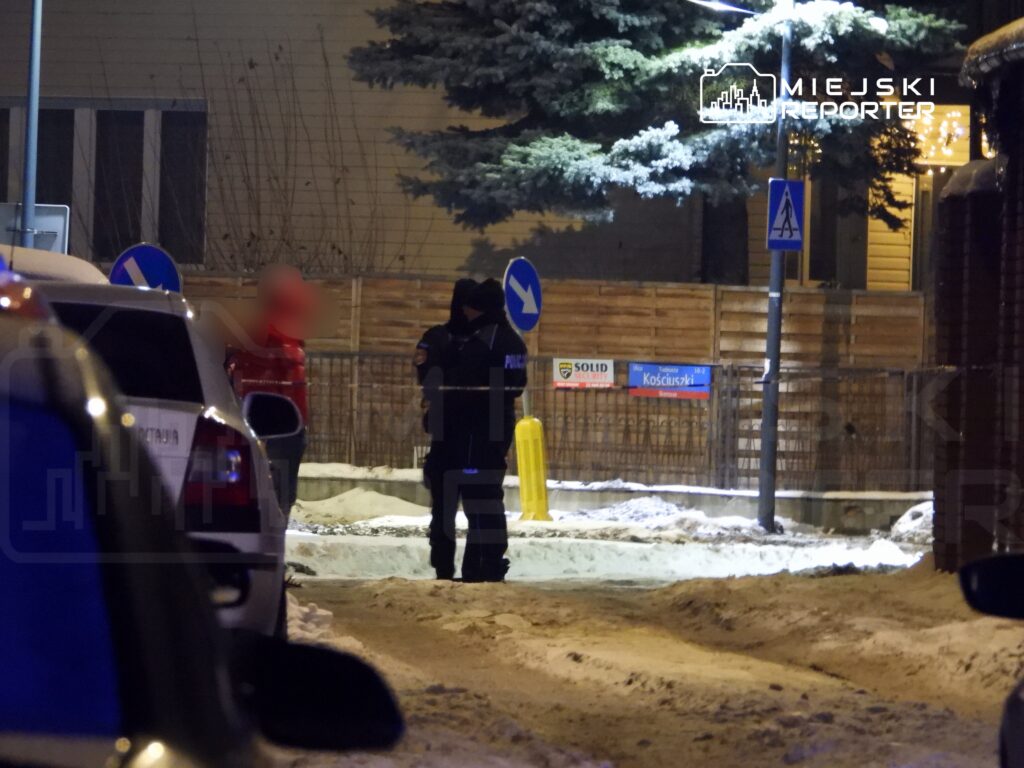 Mundurowy funkcjonariusz rozmawia z osobą w czerwonej kurtce na ośnieżonej ulicy w nocy.