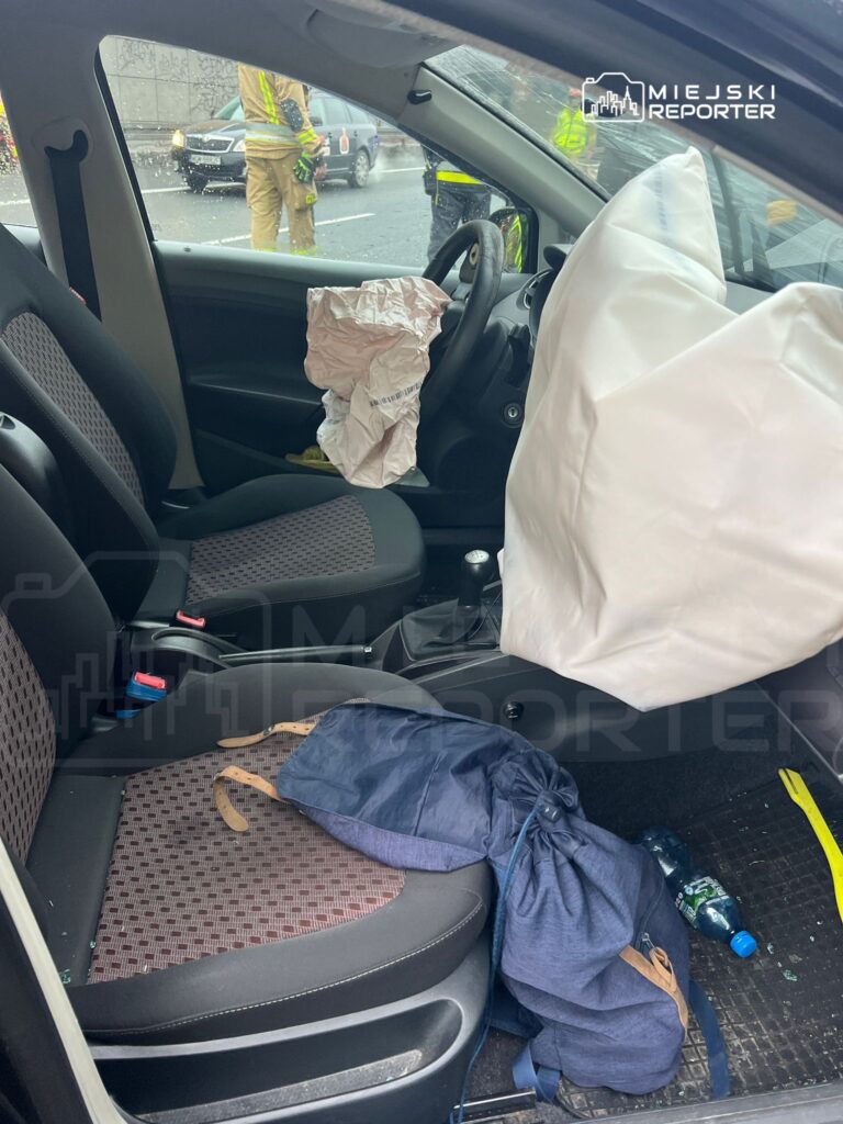Wnętrze samochodu po wypadku, z odpalonymi poduszkami powietrznymi, rozrzuconymi rzeczami osobistymi i potłuczonym szkłem.