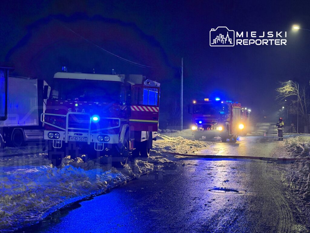 Strażacy pracują nad akcją ratunkową w nocy, obok dwóch wozów strażackich na ośnieżonej drodze.