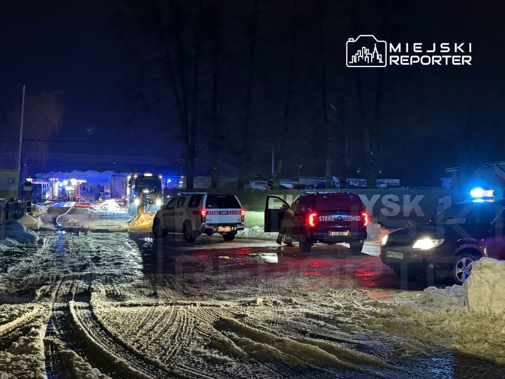 Na ośnieżonej drodze nocą stoją pojazdy służb ratunkowych z włączonymi sygnałami świetlnymi.
