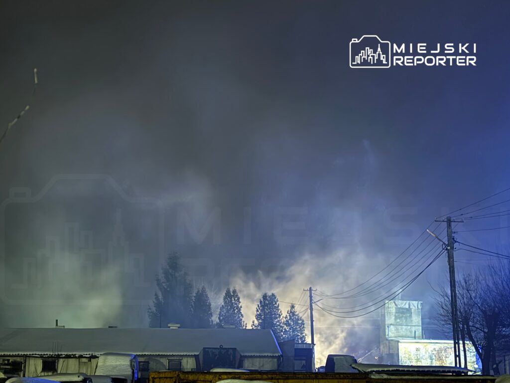 Gęsty dym unoszący się nad budynkami w mroźnej scenerii, otoczenie oświetlone niebieskim światłem.