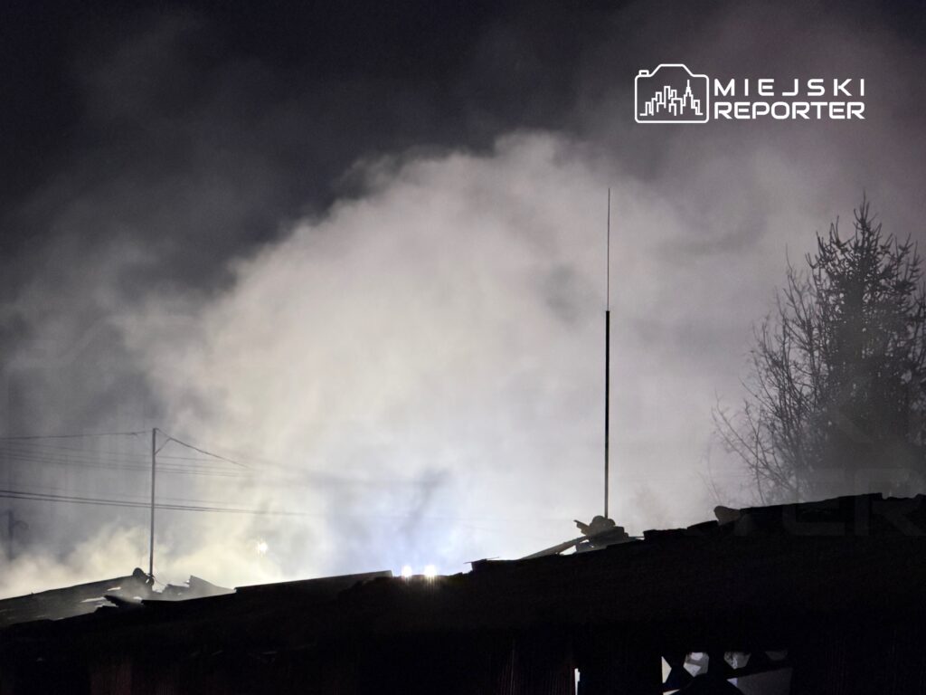 Gęsty dym unoszący się nad zniszczonym dachem budynku w ciemnej scenerii nocnej.