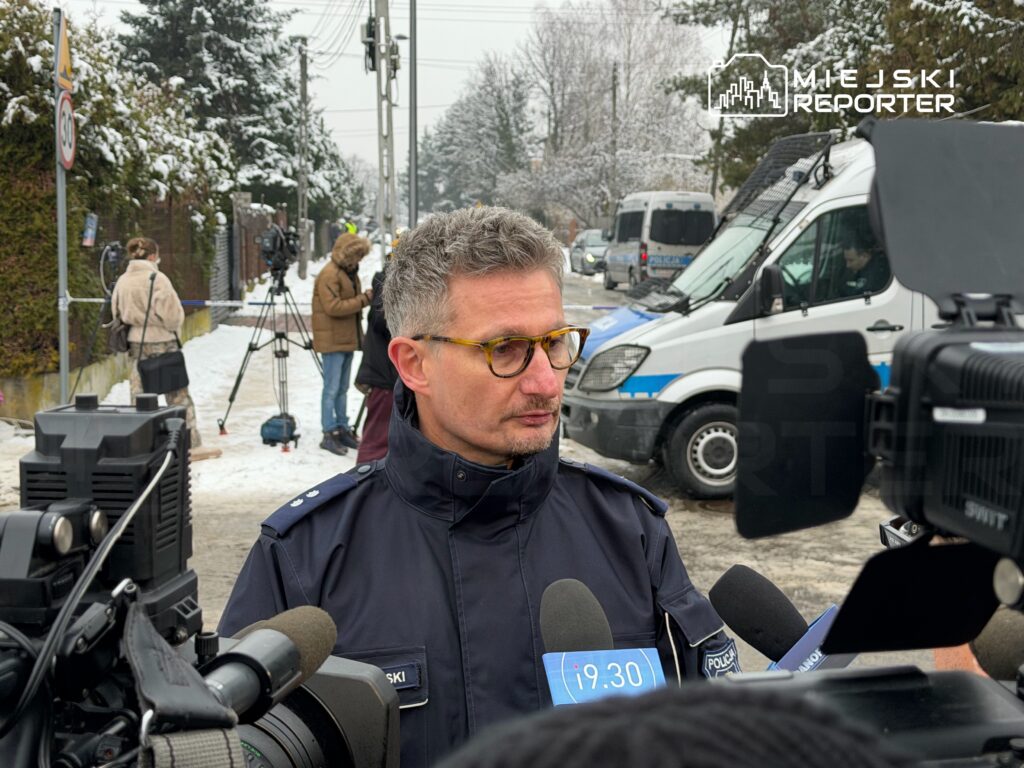 Funkcjonariusz policji w mundurze udziela wywiadu przed kamerami w zaśnieżonym otoczeniu.