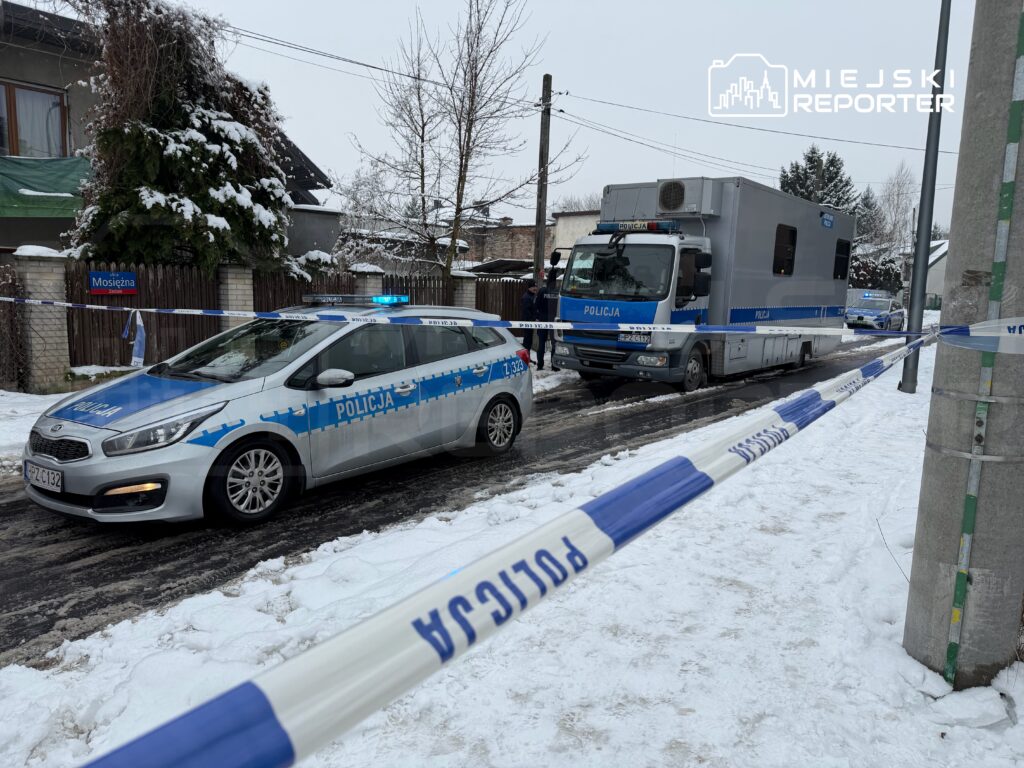 Policyjny radiowóz i pojazd operacyjny stoją na zaśnieżonej ulicy, otoczone taśmą zabezpieczającą.