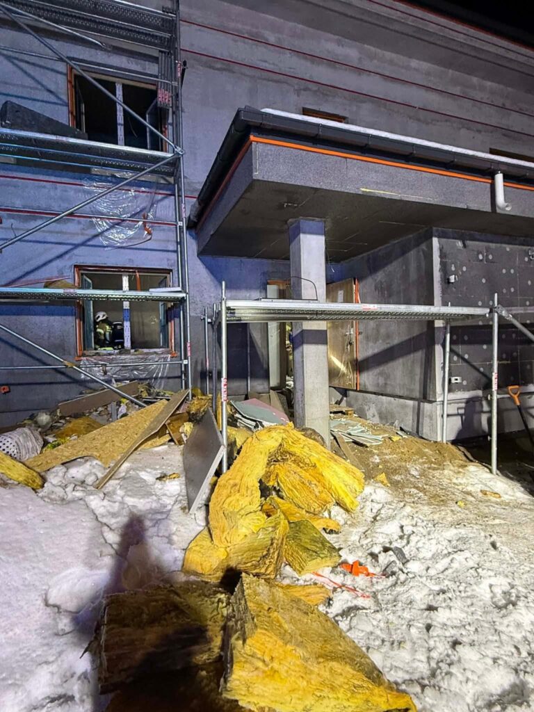 Na placu budowy leżą resztki materiałów budowlanych, obok rusztowanie i świeżo otynkowana ściana.