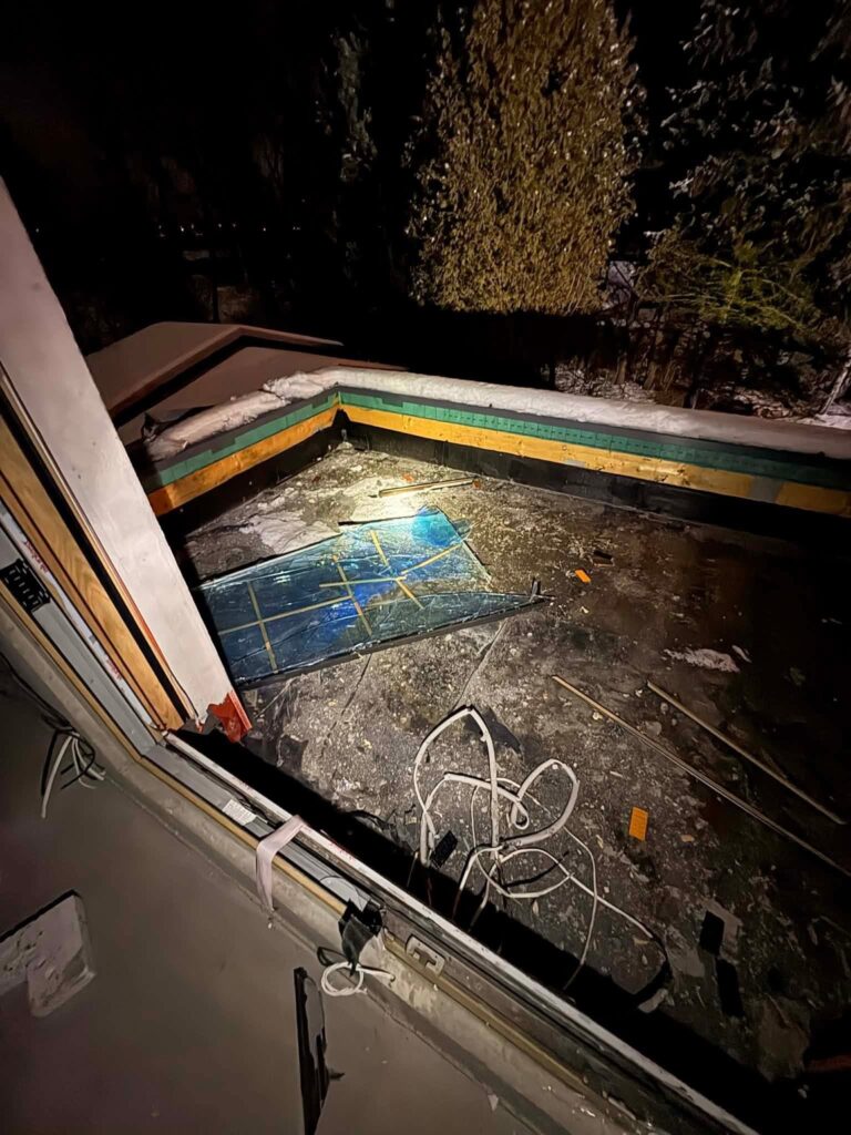 Zniszczony taras oświetlony lampą, z niebieską folią na podłożu i porozrzucanymi materiałami budowlanymi.