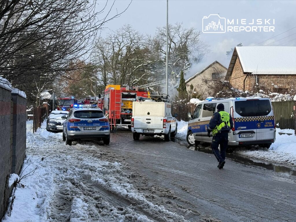 W pobliżu budynku mieszkalnego strażacy i policja interweniują w miejscu pożaru, w otoczeniu śniegu.
